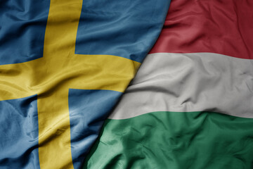 big waving national colorful flag of sweden and national flag of hungary .