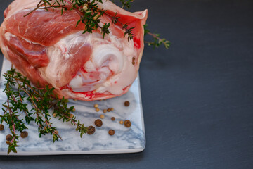 Pork knuckle.Pork meat on the bone.Pork knuckle, peppercorns, fresh thyme on a marble board on a black slate background.  - obrazy, fototapety, plakaty