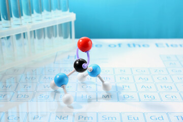 Molecular model and test tubes on periodic table against light blue background. Space for text