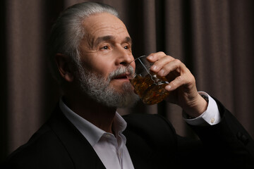 Senior man in suit drinking whiskey on brown background