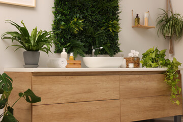 Green artificial plants, vanity and different personal care products in bathroom
