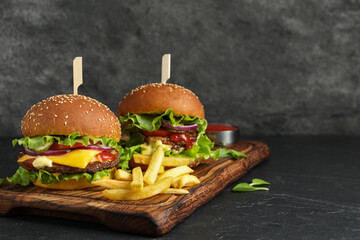 Delicious burgers with beef patty and french fries on dark table, space for text