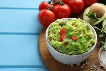 Delicious guacamole and ingredients on light blue wooden table, space for text