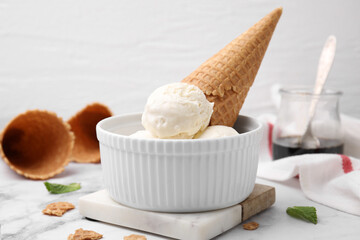 Scoops of ice cream with caramel sauce and wafer cone on white marble table, closeup