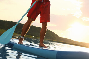 Man paddle boarding on SUP board in river at sunset, closeup