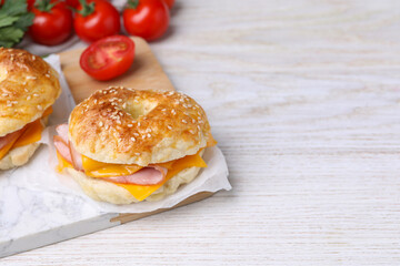 Delicious bagels with ham, cheese and products on white wooden table. Space for text