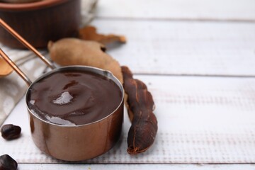 Measuring cup with tasty tamarind sauce and fresh pods on white wooden table. Space for text