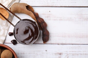 Measuring cup with tasty tamarind sauce and fresh pods on white wooden table, flat lay. Space for text