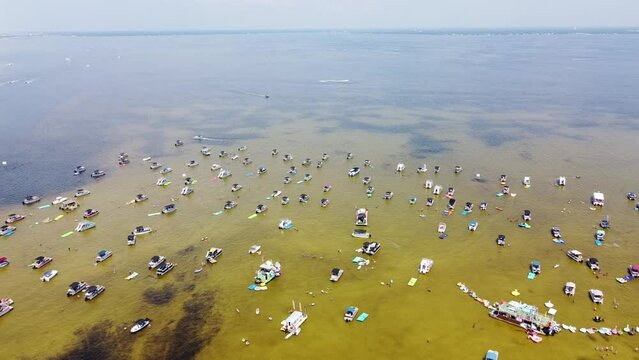 People enjoy boating, pontoons, jet skis, paddleboards, swimming, wading, sports in low tide shallow brackish water near turquoise ocean at Crab Island, Destin, Florida