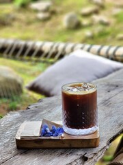 Iced americano coffee glass put on wood tray and put on old wood table. Decorate with flowers .wooden table and glass bottle and tissue paper