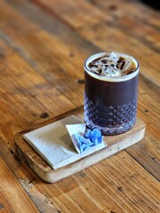 Iced americano coffee glass put on wood tray and put on old wood table. Decorate with flowers .wooden table and glass bottle and tissue paper