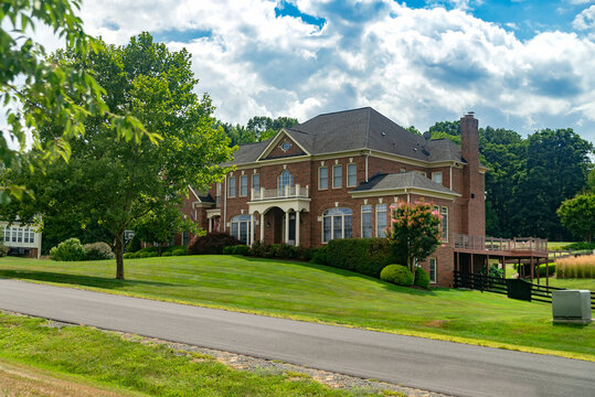 Large country brick house with landscape design near the road.