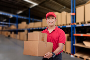 A young asian delivery man or employee inside a storage depot or warehouse facility or logistics hub. A courier handling and delivering packed parcels to be shipped.