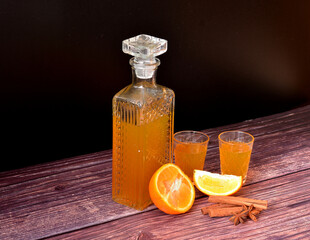 Orange liqueur on a dark wooden table, a bottle and two glasses with homemade alcohol, cinnamon and anise.