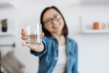 Tumbler glass with clean liquid reached out by asian woman