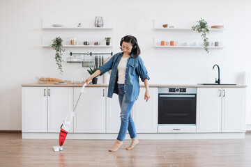 Asian lady using upright vacuum with music in headphones