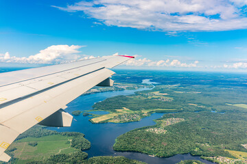 Fototapeta premium View of airplane wing, blue skies and green land during landing. Airplane window view.
