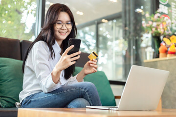 Young Asian woman holding credit card and mobile phone for electronic payment in internet online remote store. - obrazy, fototapety, plakaty