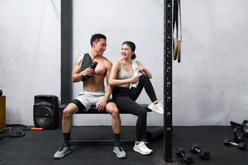 Fototapeta na wymiar Active adult couple resting on a workout bench in a vibrant modern gym, representing health, fitness, and partnership.