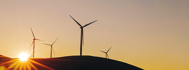 Banner with wind turbines in back light of rising sun. Sustainable wind energy background.