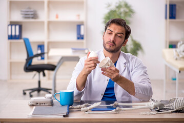 Young male doctor studying human skeleton at the hospital