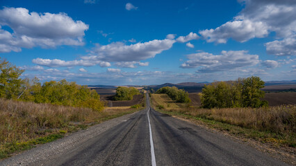 Road landscape. Empty track among mountains and fields in autumn. 