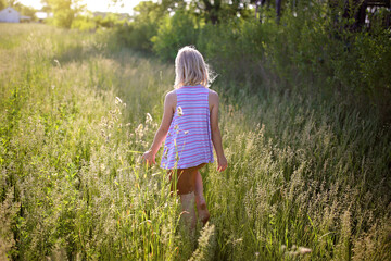 Naklejka na ściany i meble Young Girl Walking Through Country Field at Golden Sunset