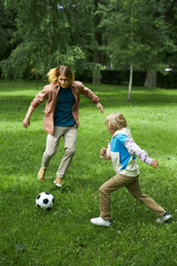 Vertical action shot of father and son playing football together on green grass