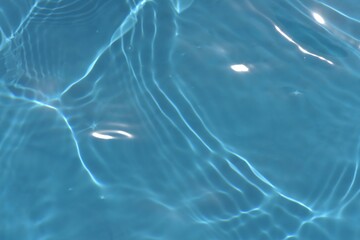 Blue water with ripples on the surface. Defocus blurred transparent blue colored clear calm water surface texture with splashes and bubbles. Water waves with shining pattern texture background.