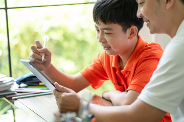 Asian father and son using tablet teaching son to draw.playing with digital tablet at desk fatherhood