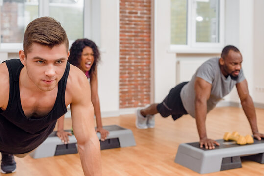 Portrait of happy diverse people practicing push-ups exercise in modern gym, Upbeat image of a diverse group of individuals engaging in push-up exercises within a contemporary fitness facility.