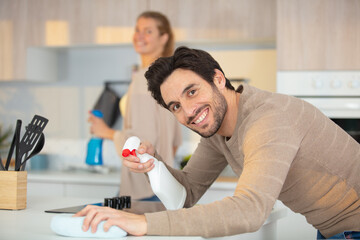 cheerful man holding rag while cleaning kitchen table