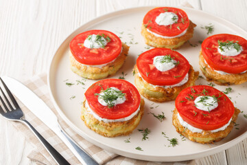 Homemade fried zucchini in egg batter served with creamy garlic sauce, dill and fresh tomatoes close-up in a plate on the table. Horizontal