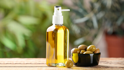 Spray bottle with cooking oil and olives on wooden table against blurred background, closeup