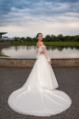 Beautiful bride in wedding dress posing on sunset near lake