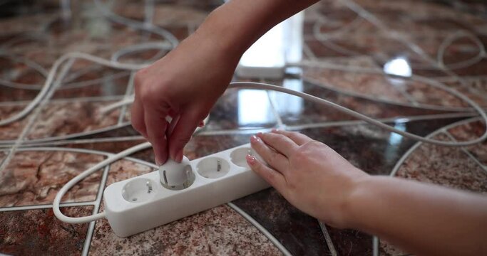 Woman hand inserts electric plug into white socket. Connecting electrical devices