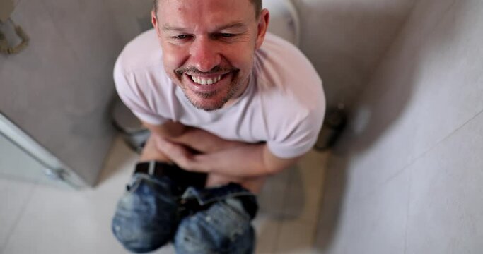 Portrait of young contented man sitting on toilet. laxative for adult. Laxative for adult