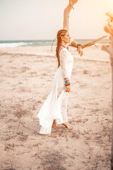 Fototapeta na wymiar woman sea white dress. Model in boho style in a white long dress and silver jewelry on the beach. Her hair is braided, and there are many bracelets on her arms.