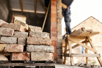 Selective focus on pile of bricks on a reconstruction area with builder building a house.