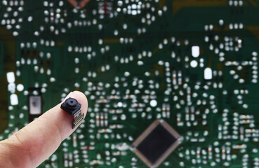 Finger showing a miniature digital camera with a background of electronic circuitry
