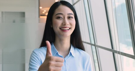 Attractive Asian businesswoman showing thumbs up gesture, happy client give positive feedback, feels satisfied with received services, applicant passed job interview, get hired enjoy moment of success