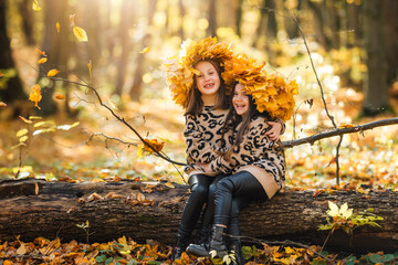 Children play with dry yellow maple leaves in the autumn forest. Children sit on fallen tree in the...