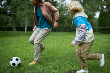 Candid shot of father and son running in park together and playing football on green grass