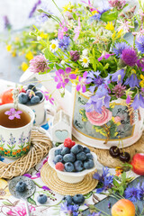 Still life with meadow flowers bouquet, berries and cup of tea in natural light, vivid wild flowers, berries on table with wicker small trays, close up view