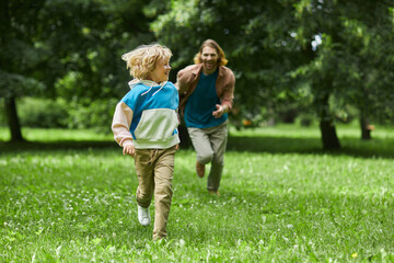 Carefree portrait of father and son running towards camera playing chase in park, copy space
