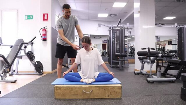 Trainer corrects woman's back posture during gym stretch