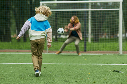 Back view of little boy playing football with father and scoring goal, copy space