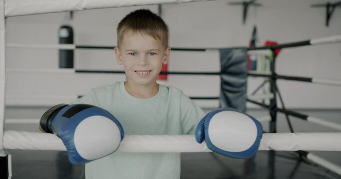 Slow motion portrait of happy child young boxer wearing gloves standing in ring smiling looking at camera. Childhood and sports education concept.