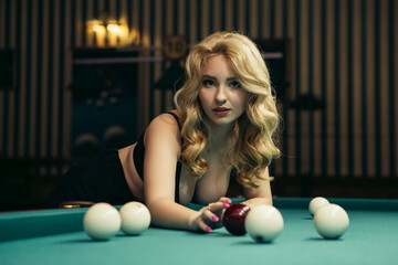 Blond woman playing enjoying billiard, hold billiard balls on table with green surface in billiard...