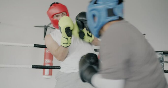 Professional boxers men wearing helmets and gloves training in modern gym throwing punches concentrated on fight. People and martial arts concept.